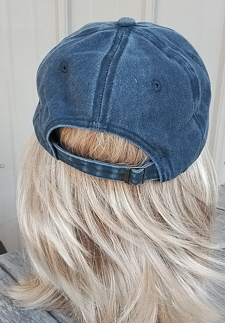 Mannequin head with blonde wig wearing a blue denim cap on a wooden surface.