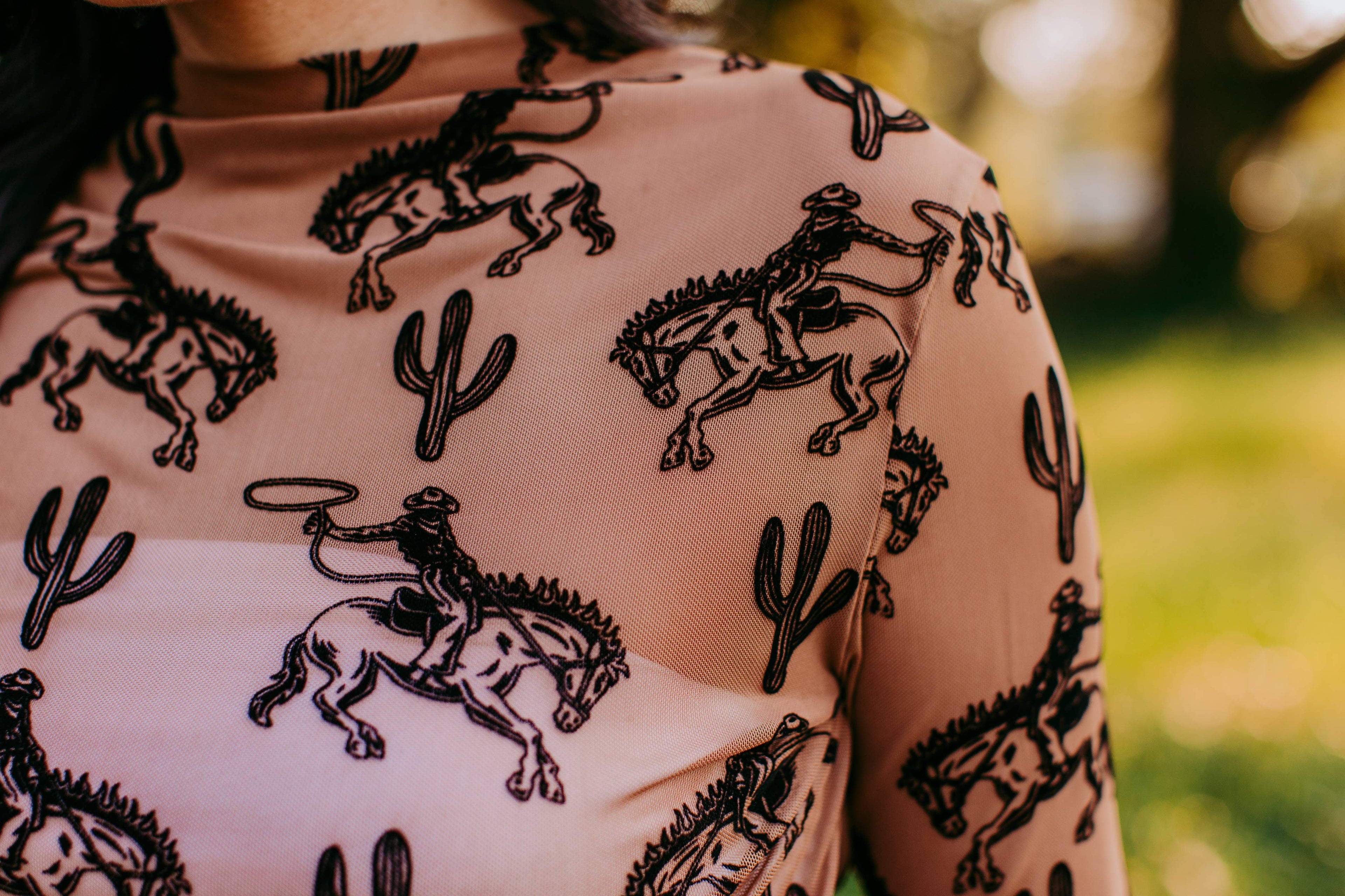 Close-up of a beige fabric with black cowboy and cactus patterns, blurred green background