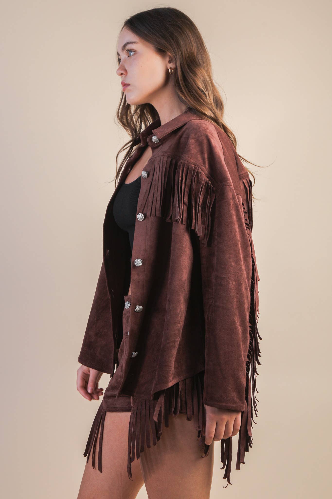 Woman wearing a brown suede fringe jacket against a plain background