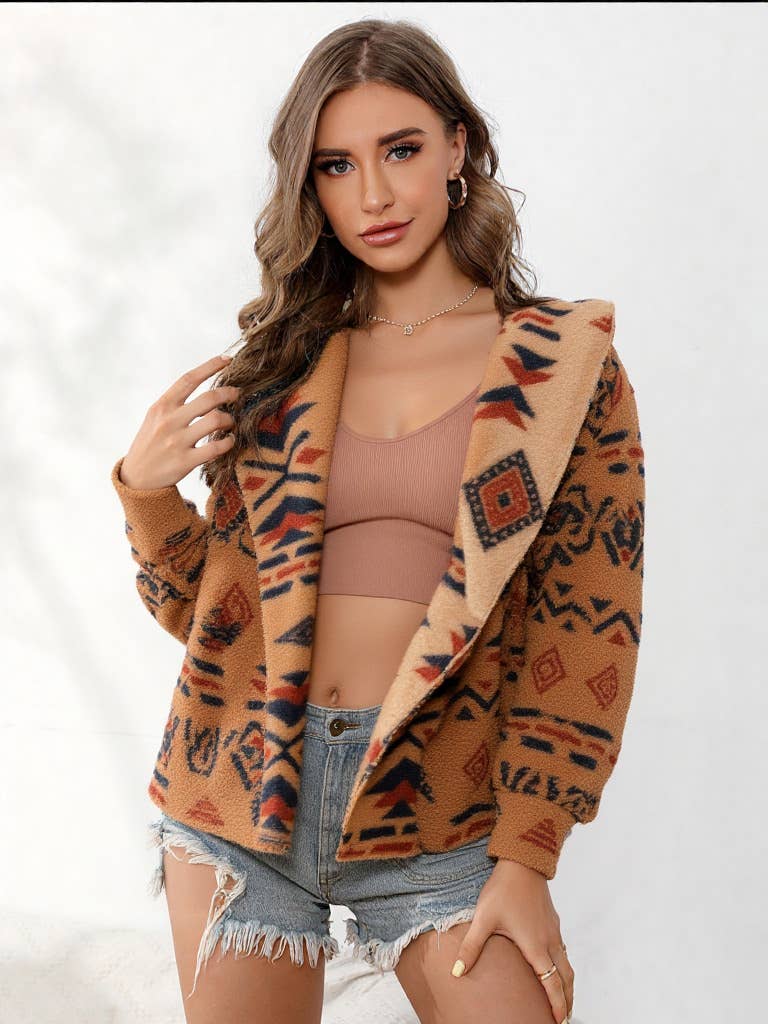 Woman wearing a patterned jacket over a beige top and denim shorts on a white background