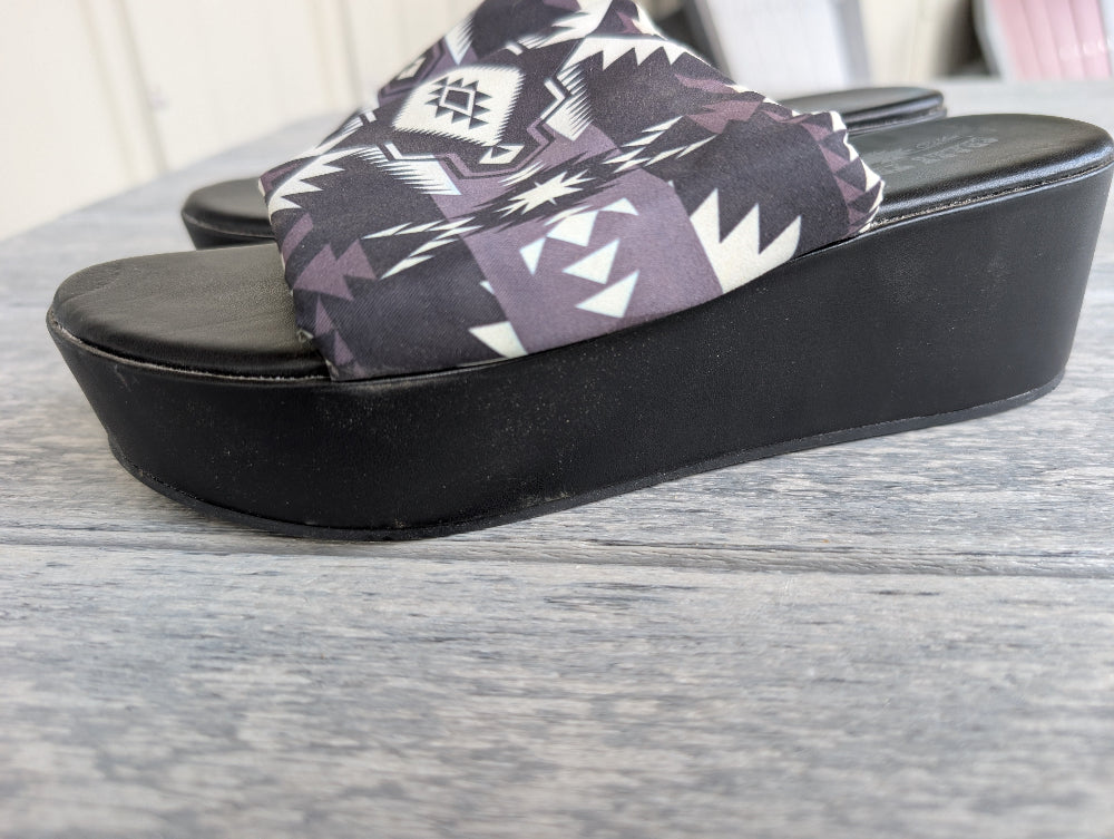 Black wedge sandal with patterned strap on a wooden surface