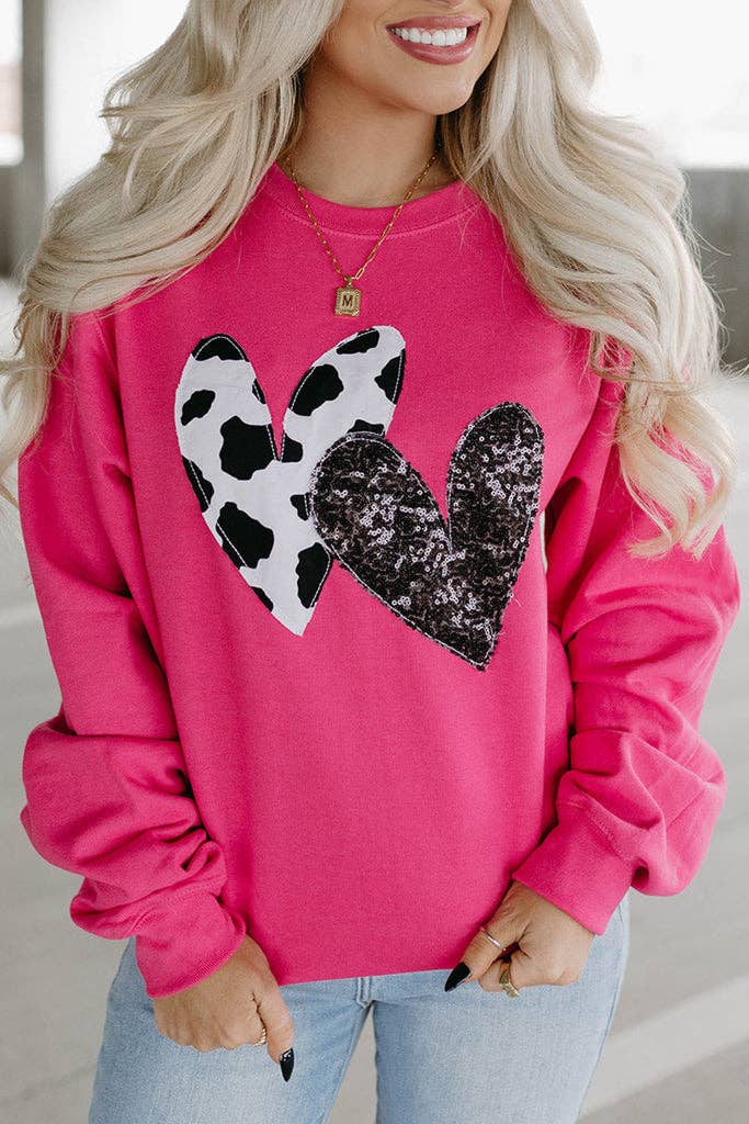 A woman wearing a pink sweatshirt with a cow and sequin double heart patch on the front.