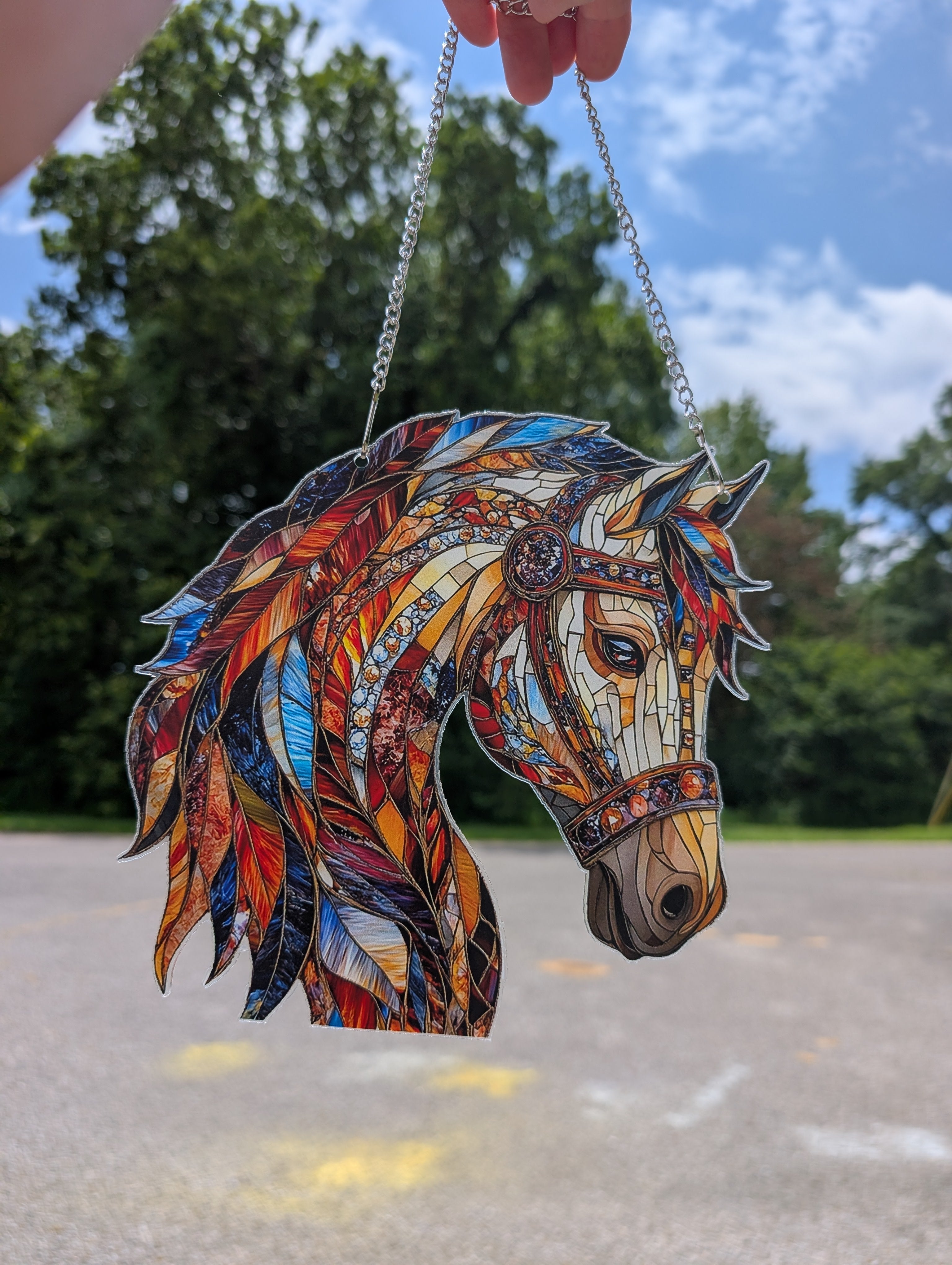 Colorful mosaic horse head ornament held by a hand against a natural background.