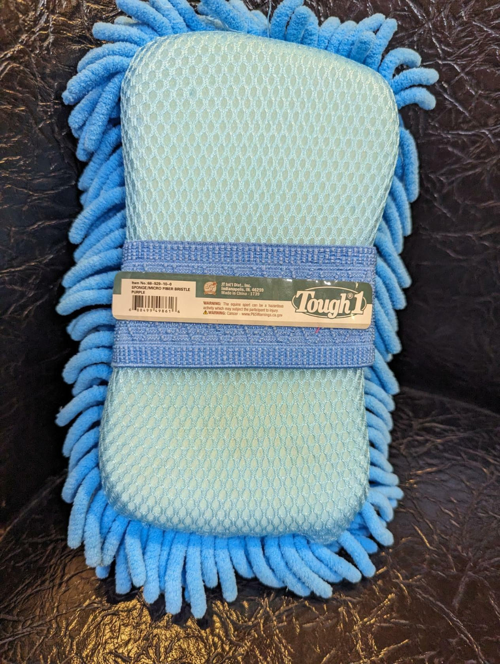 Blue microfiber cleaning mitt with a brand label on a dark textured surface