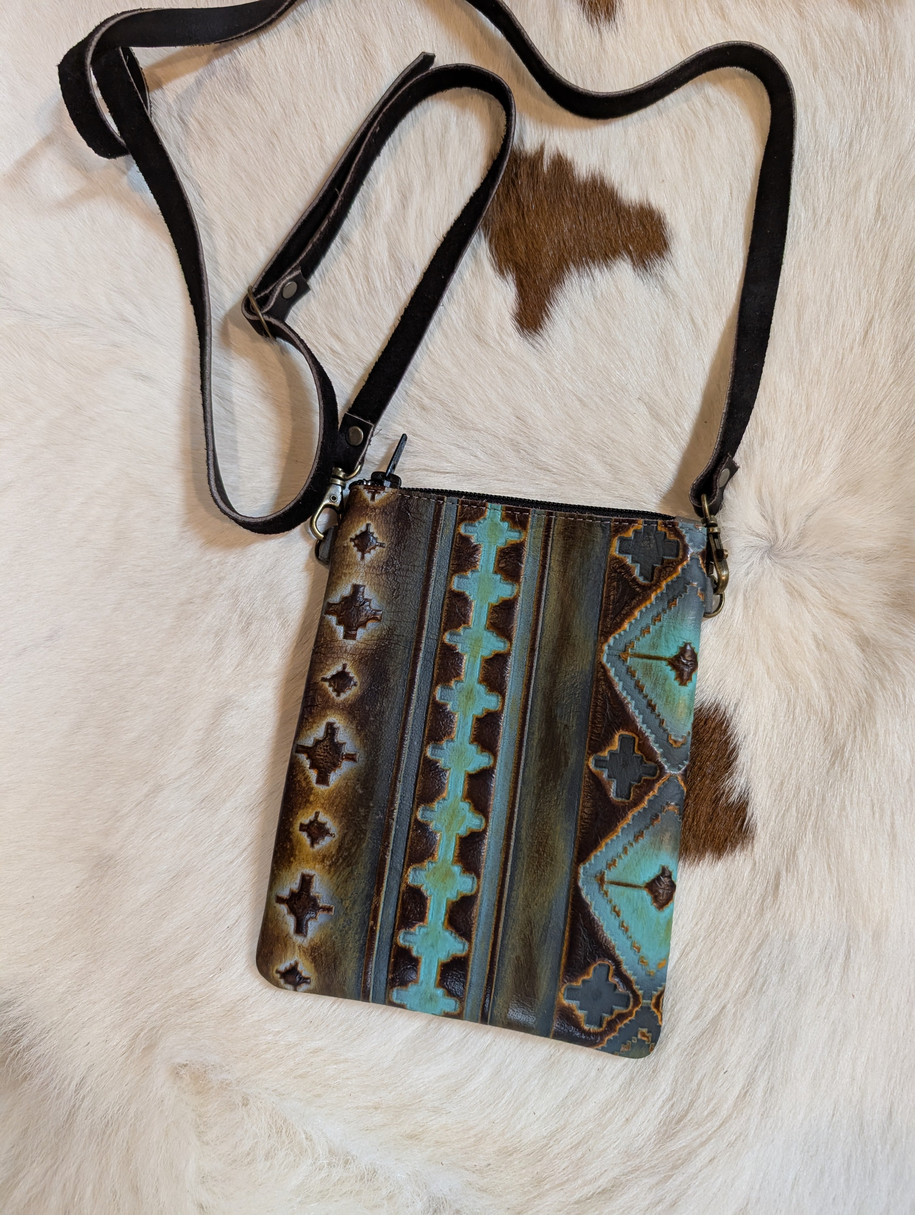 Genuine leather handmade crossbody bag in western tooled style, displayed on rustic wooden surface.