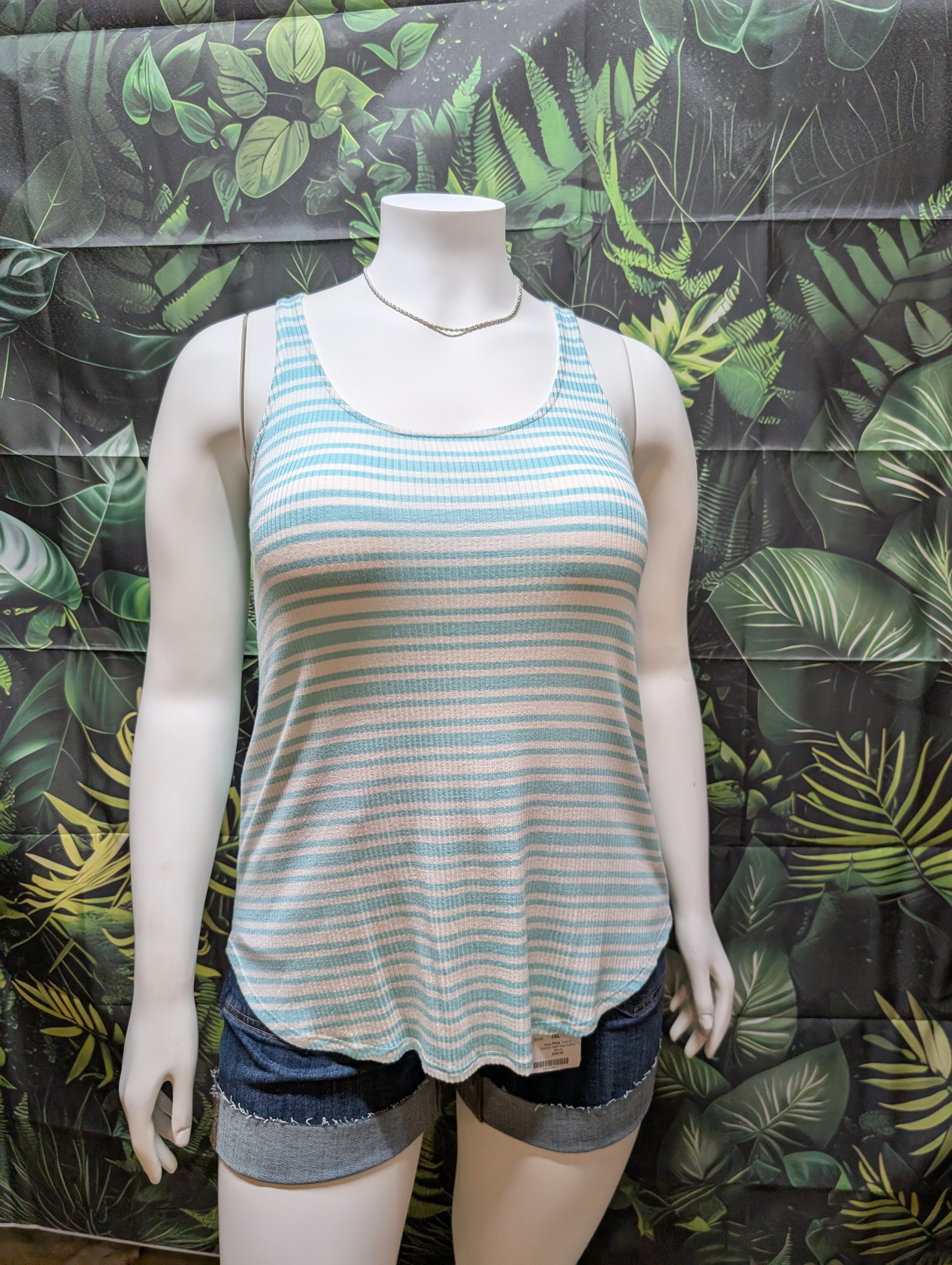 Mannequin wearing a striped tank top and shorts against a tropical leaf patterned backdrop