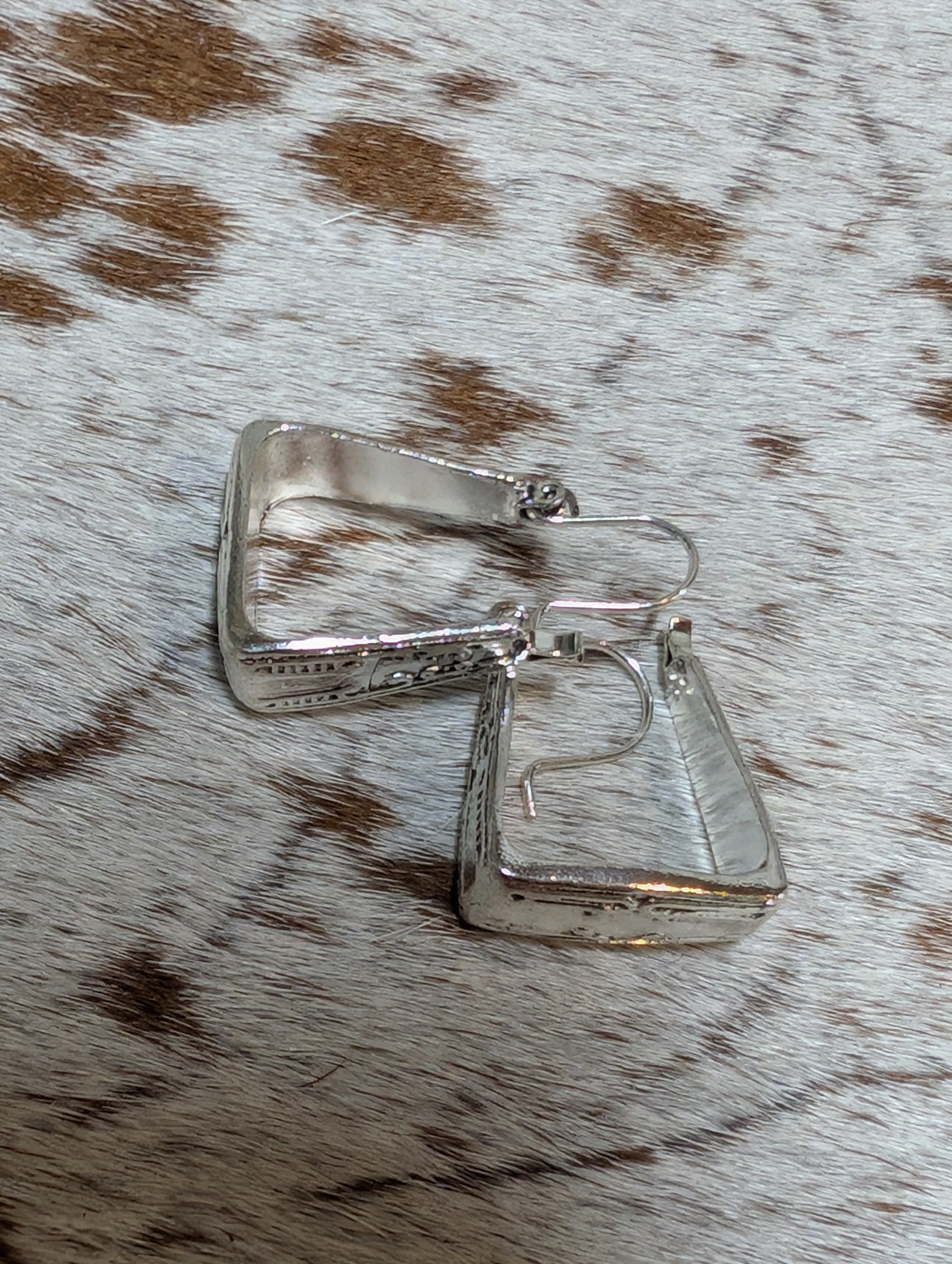 Silver square earrings on a brown and white fur surface