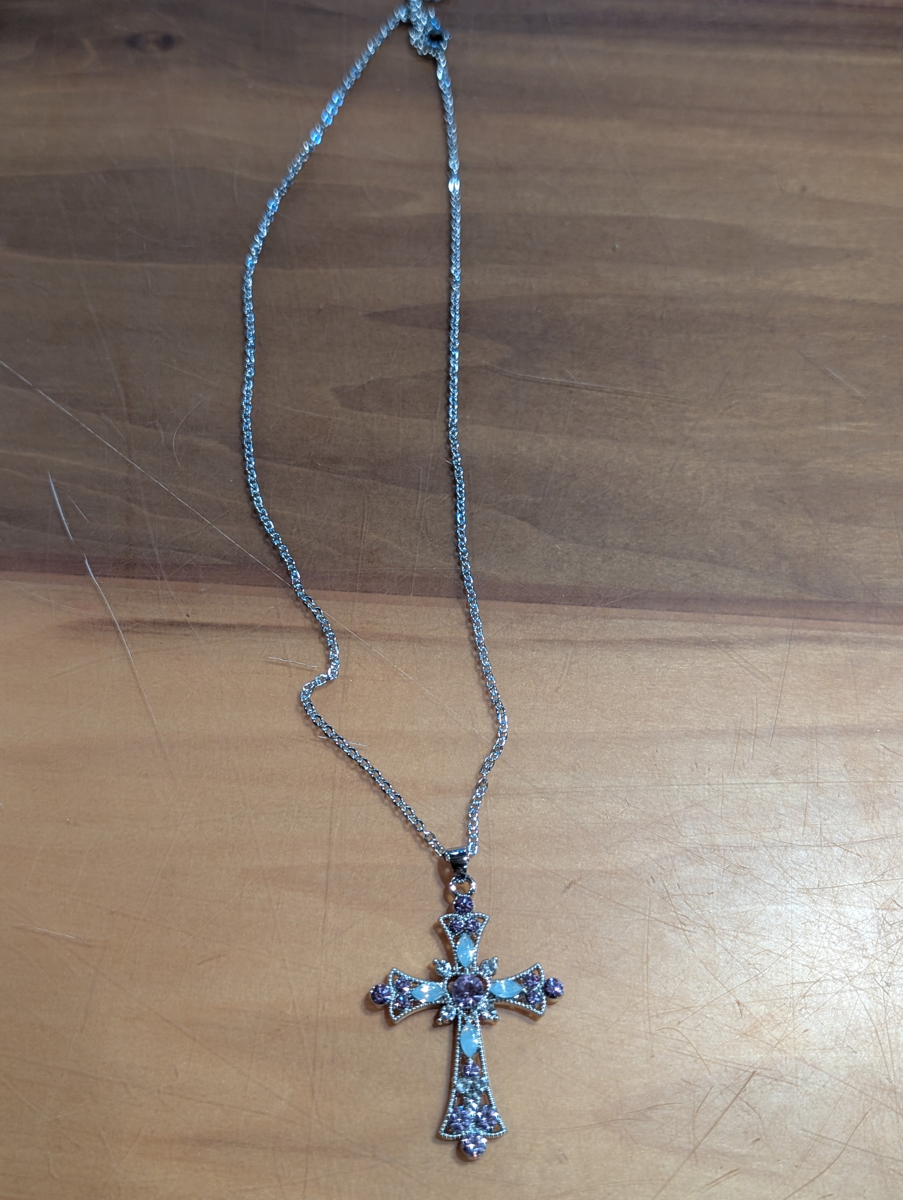 Silver cross necklace with purple stones on a wooden surface