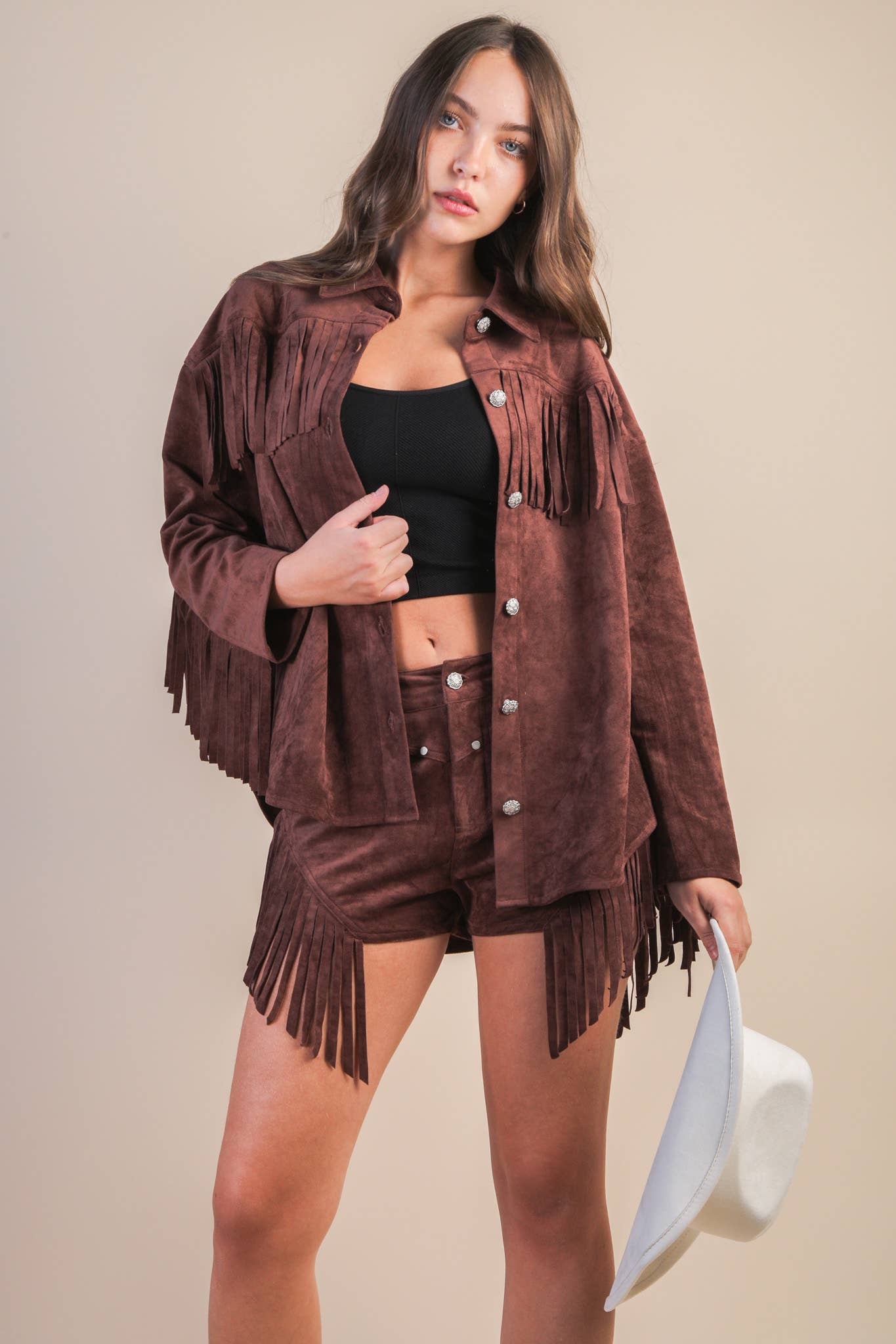 Woman wearing a brown suede fringe jacket and skirt set on a beige background