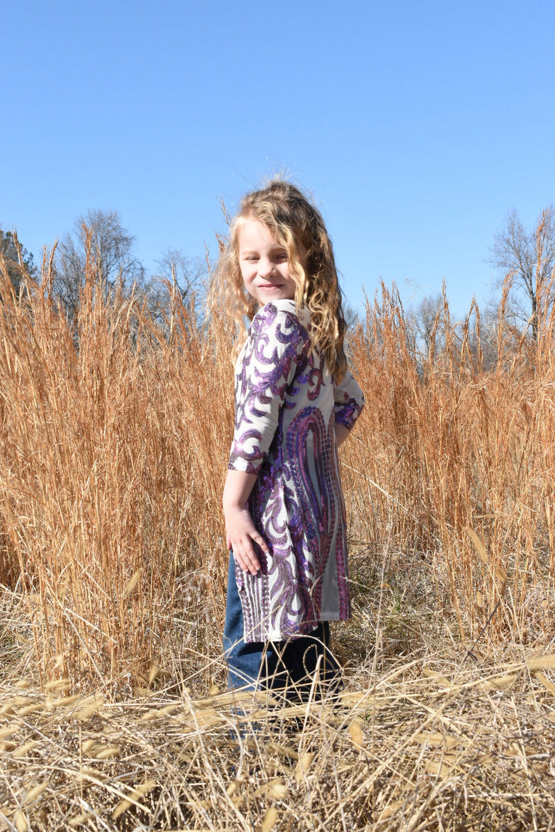 Young girl standing in brown grass wearing a western purple and white duster.