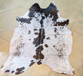 Cowhide rug WITH DARK BROWN AND WHITE PATCHES ON A TAN FLOOR.