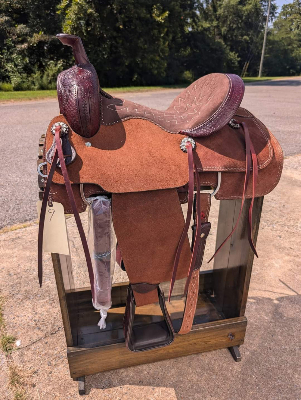Brown leather saddle on a wooden stand outdoors