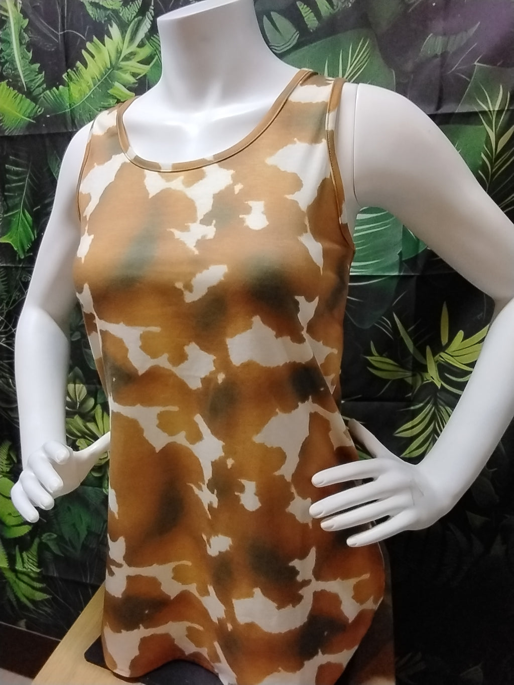 Mannequin wearing a sleeveless dress with a brown and white pattern against a leafy background