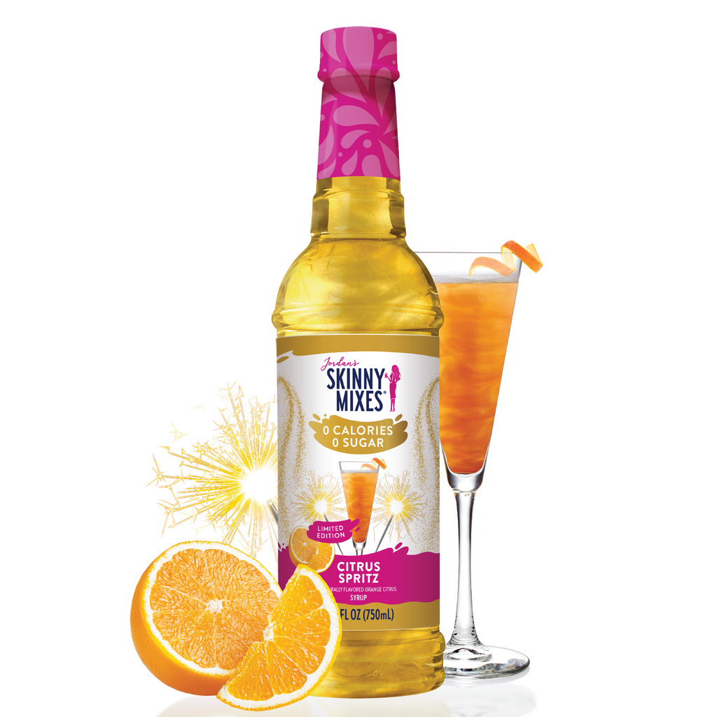 Bottle of Skinny Mixes Citrus Spritz with a glass of orange juice and oranges on a white background