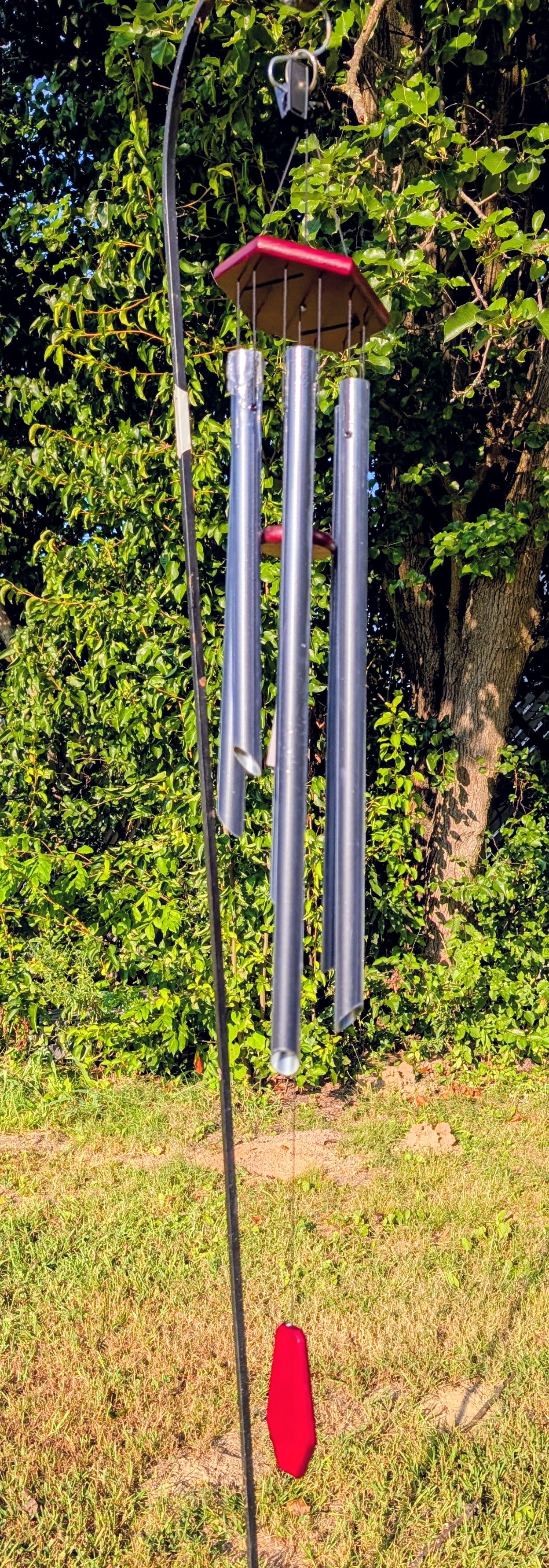 Metal wind chime with red accents in a grassy area with trees in the background