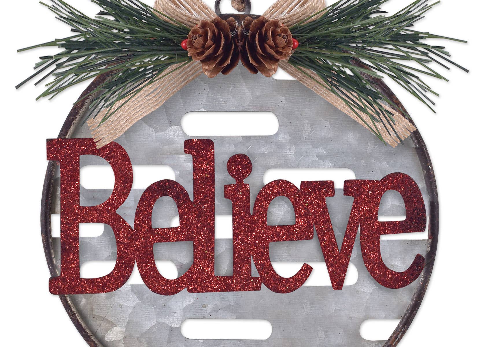 A oval holiday ornament featuring the word "Believe" in glittery red letters over a galvanized metal background, decorated with pine branches, two pinecones, and a tan ribbon bow at the top.