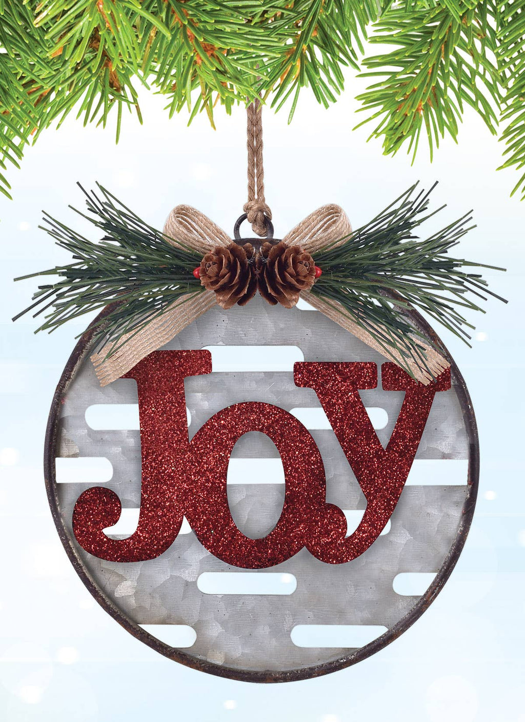 A round Christmas ornament hanging from a pine branch. The ornament has a distressed dark metal rim, a gray slotted center, green pine branches, a beige ribbon bow with two small pinecones, and a glittery red "Joy'" in the center.