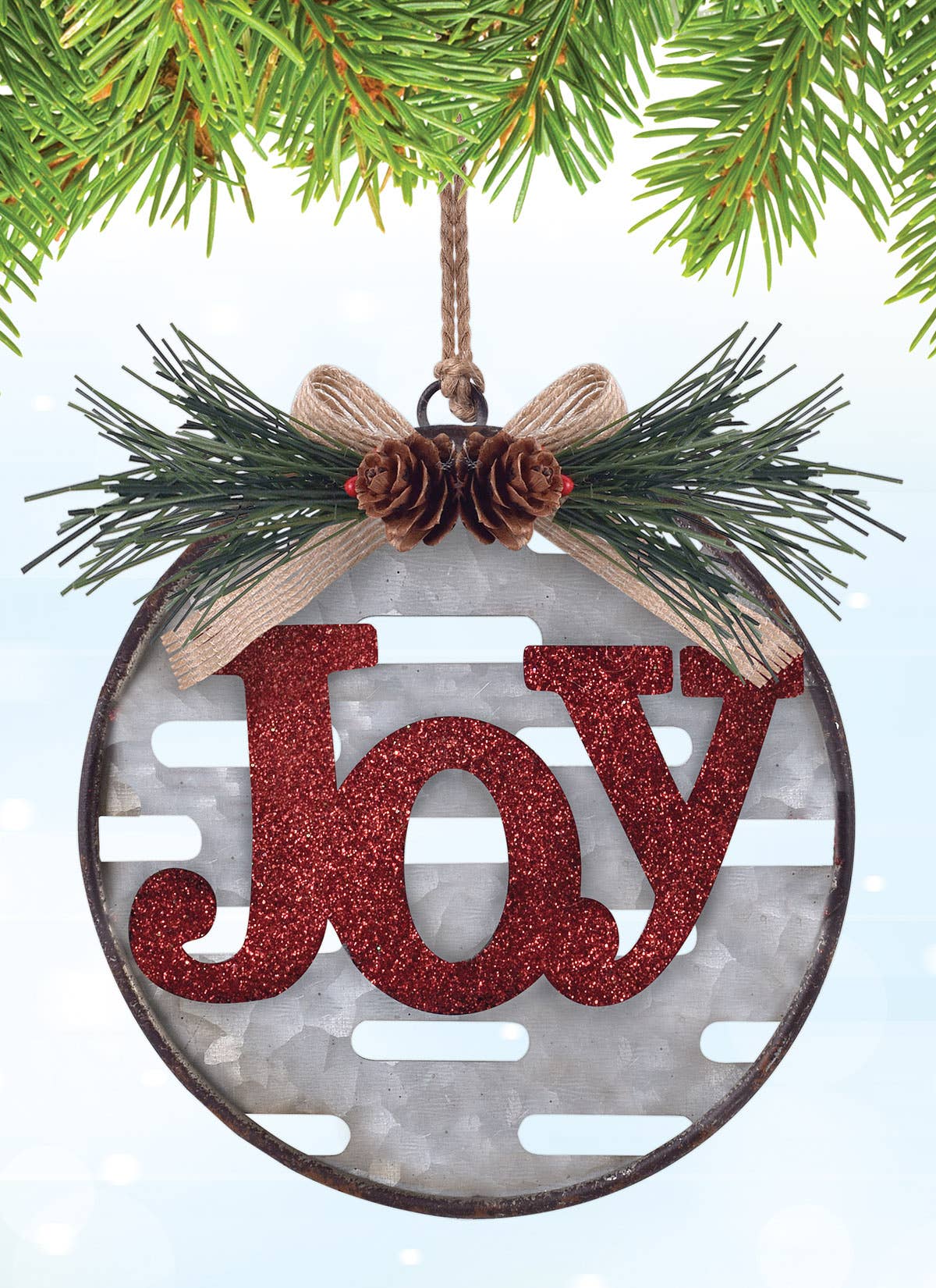 A round Christmas ornament hanging from a pine branch. The ornament has a distressed dark metal rim, a gray slotted center, green pine branches, a beige ribbon bow with two small pinecones, and a glittery red "Joy'" in the center.