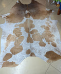 A full cowhide rug with a mix of blonde and grey spots, laid out on a floor.
