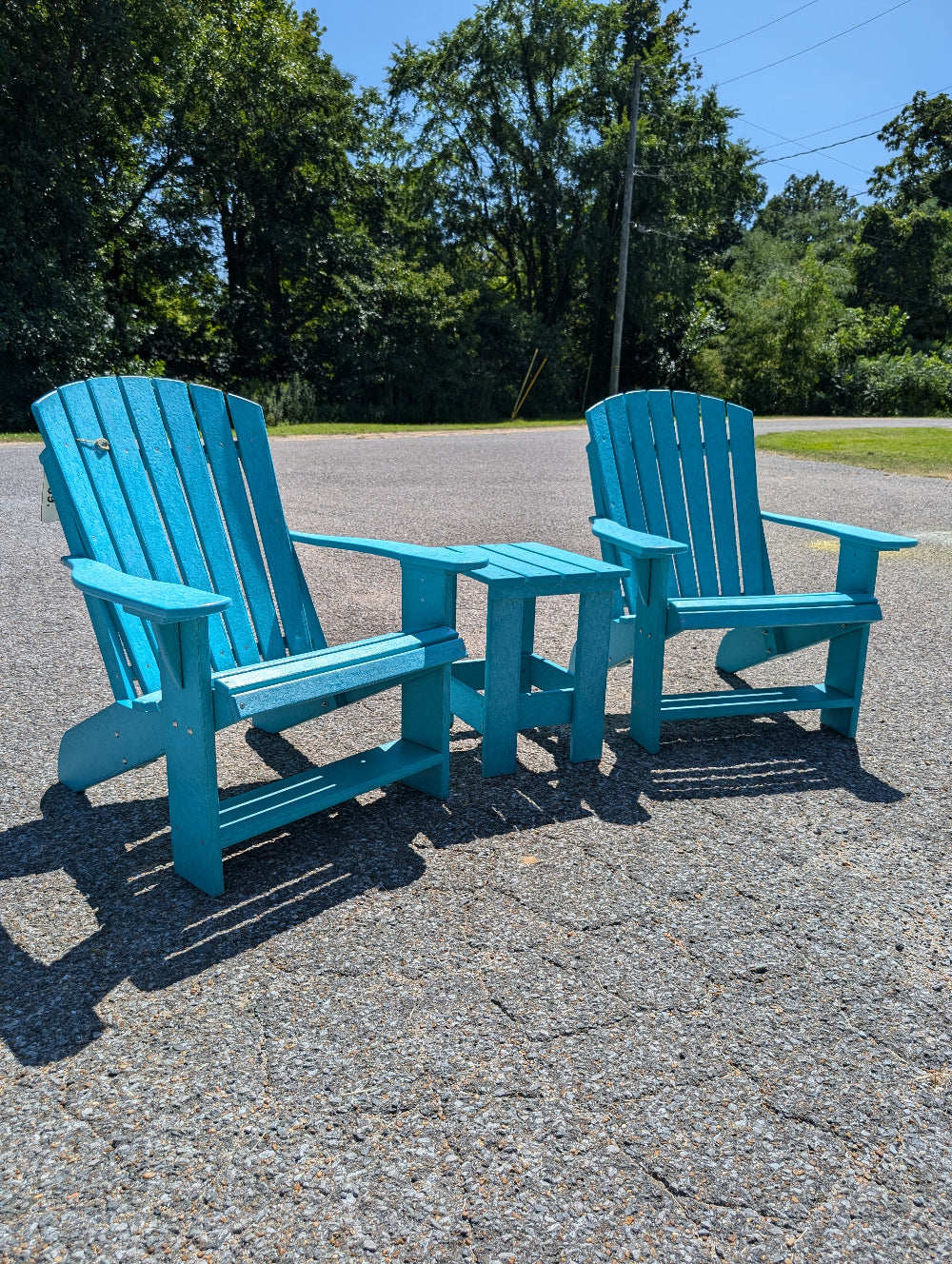 Two blue Adirondack chairs on a paved surface with trees in the background.