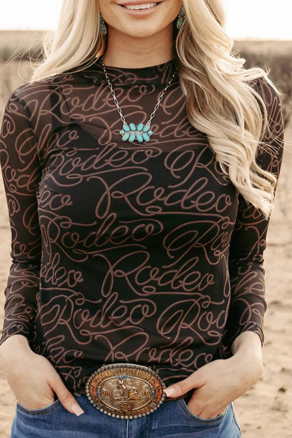 Woman wearing a mesh long-sleeve top with 'Rodeo' print and a belt buckle, standing outdoors.