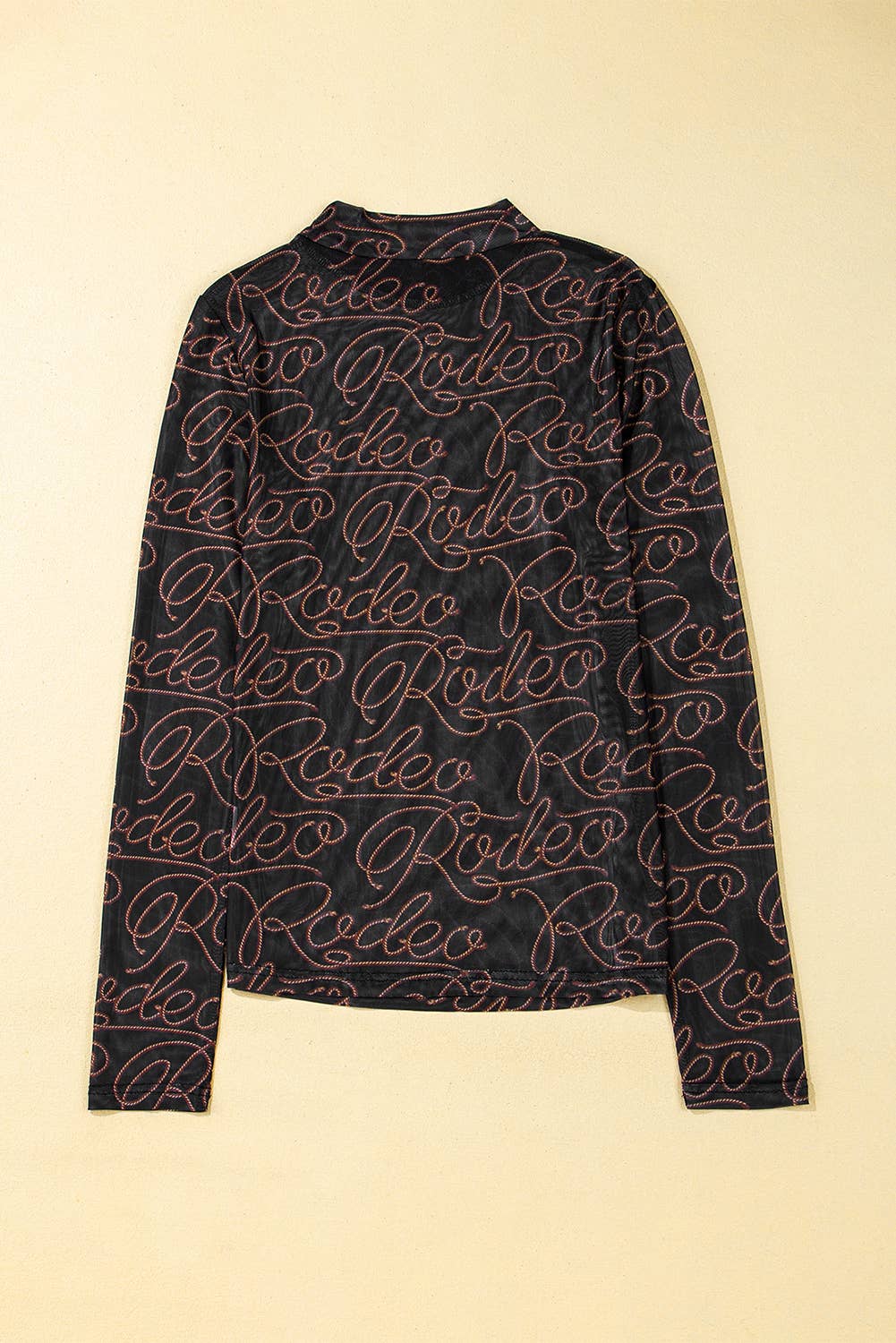 Black long-sleeve shirt with 'Rodeo' pattern on a beige background