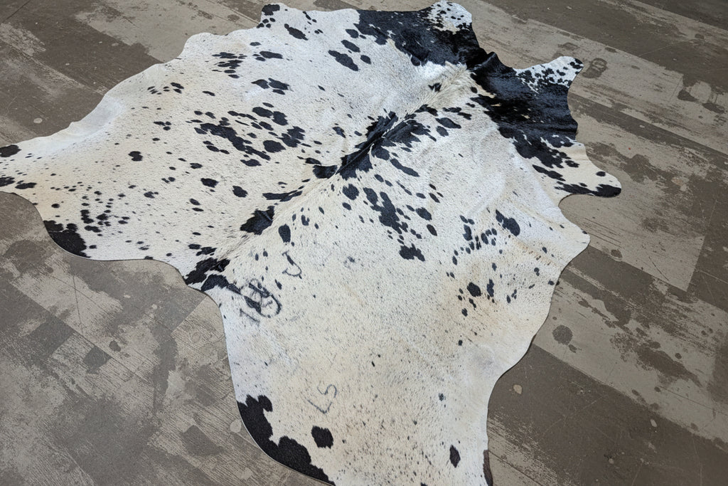 Cowhide rug with black and white pattern on a gray rustic floor.