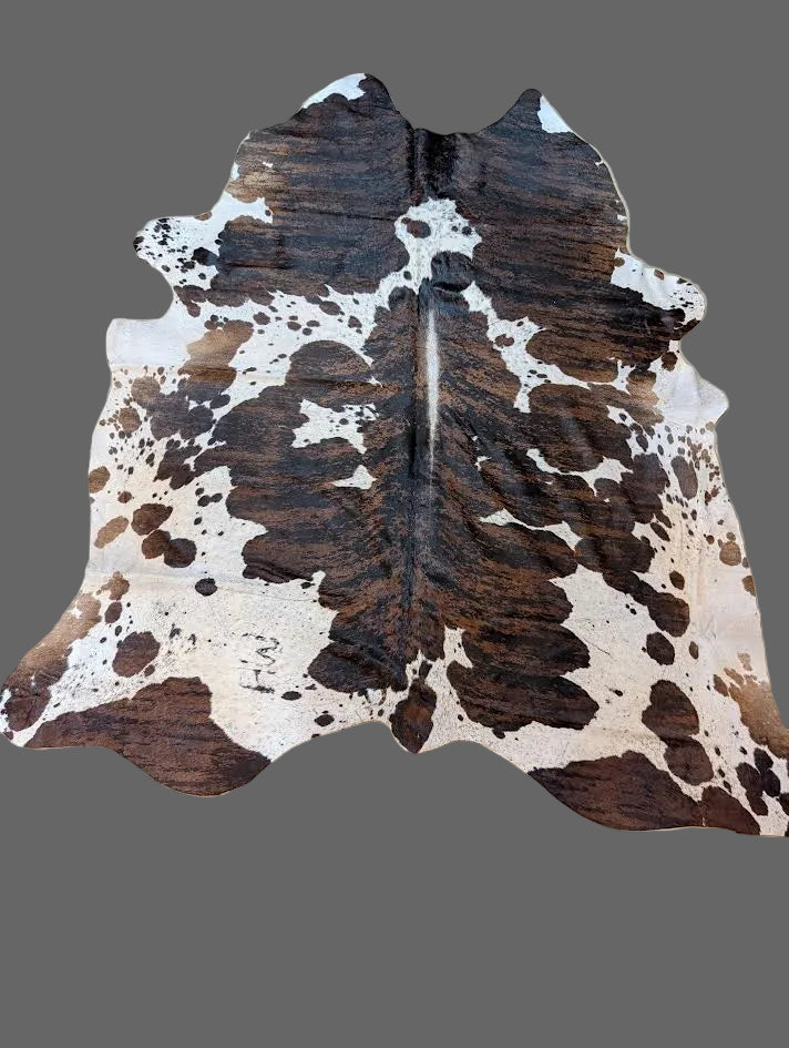 Brindle and white cowhide rug with a gray background.