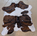 Brown and white cowhide rug on a beige floor.