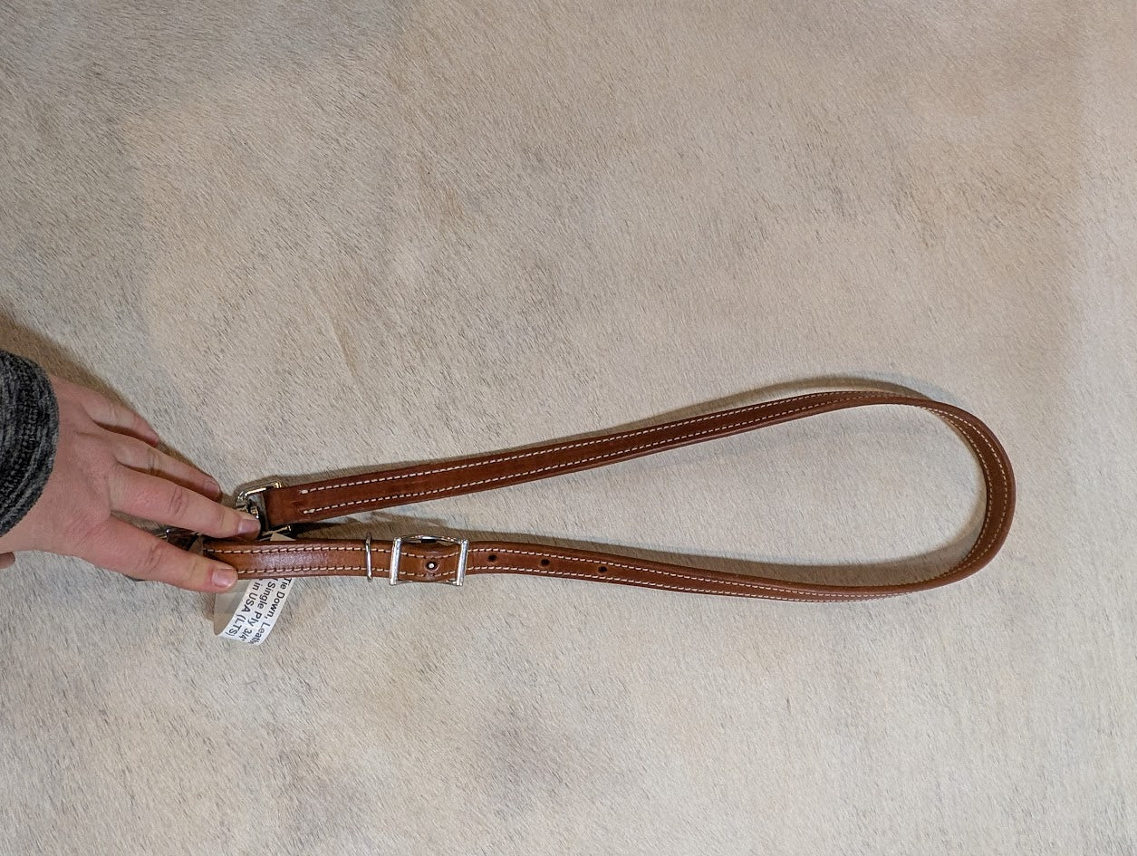 Brown leather strap with a metal buckle held by a hand on a beige carpet.
