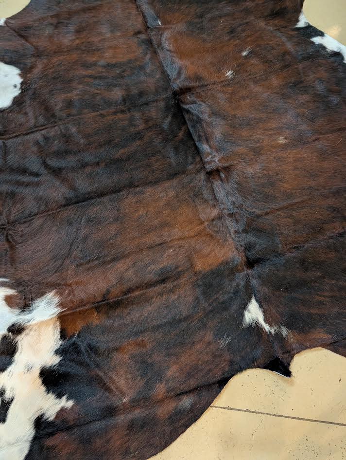 Close-up of a cowhide rug with brown, black, and white pattern on a beige floor.