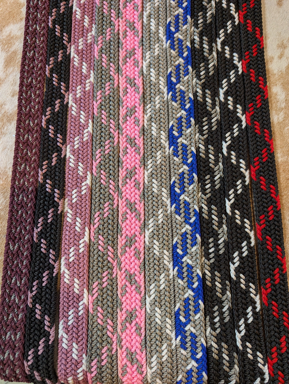 Collection of woven belts with various patterns and colors on a textured surface.