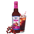 Bottle of Skinny Mixes Cherry Cola syrup with a glass of cherry cola and cherries on a white background