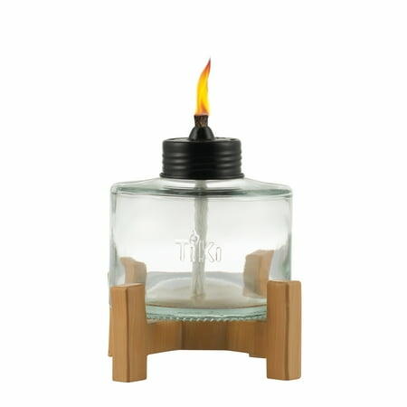 Clear glass TIKI Brand 5-inch table torch with natural raised resin base, shown unlit on an outdoor table.