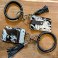 Two cowhide cardholder bangles with leather straps and black tassels, placed on a wooden surface.