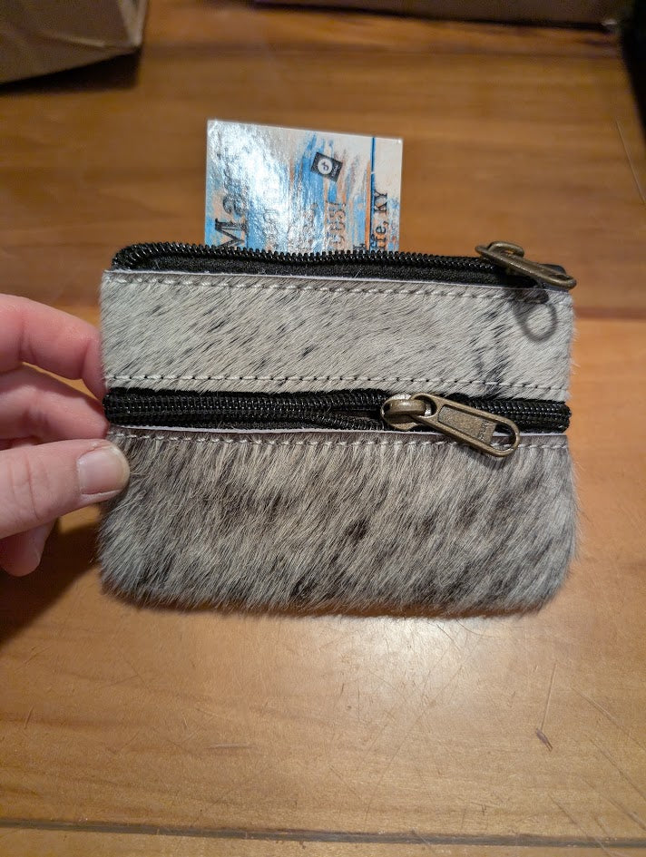 Small cowhide coin pouch with a zipper held by a hand on a wooden surface