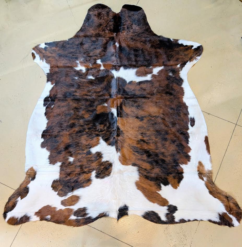 Brindle and white cowhide rug on a tan tile floor.