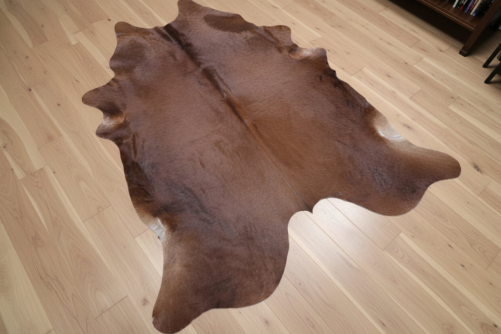 Brown cowhide rug laying diagonally on a wood floor.