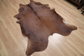 Brown cowhide rug laying diagonally on a wood floor.
