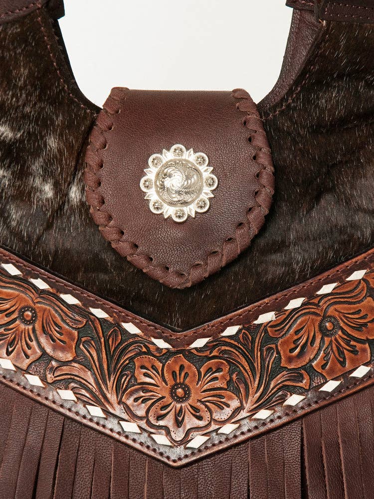 Close-up of a brown leather bag with cowhide and buckstitch designs and a decorative clasp.