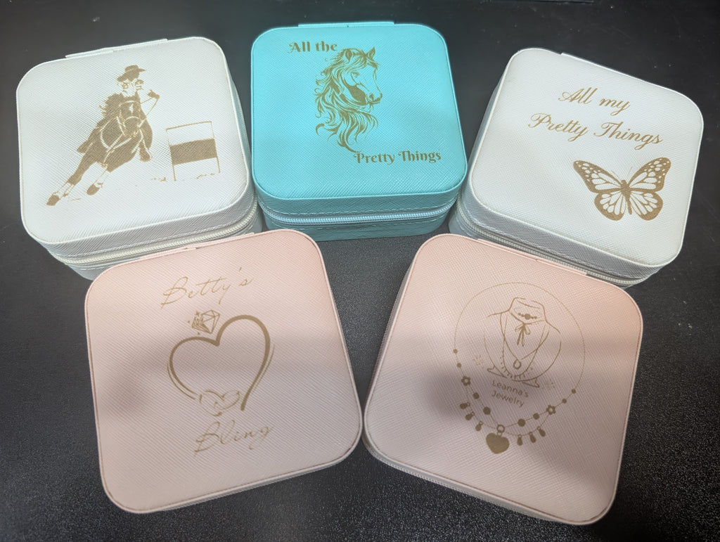 Five small square containers with gold embossed designs on a dark surface