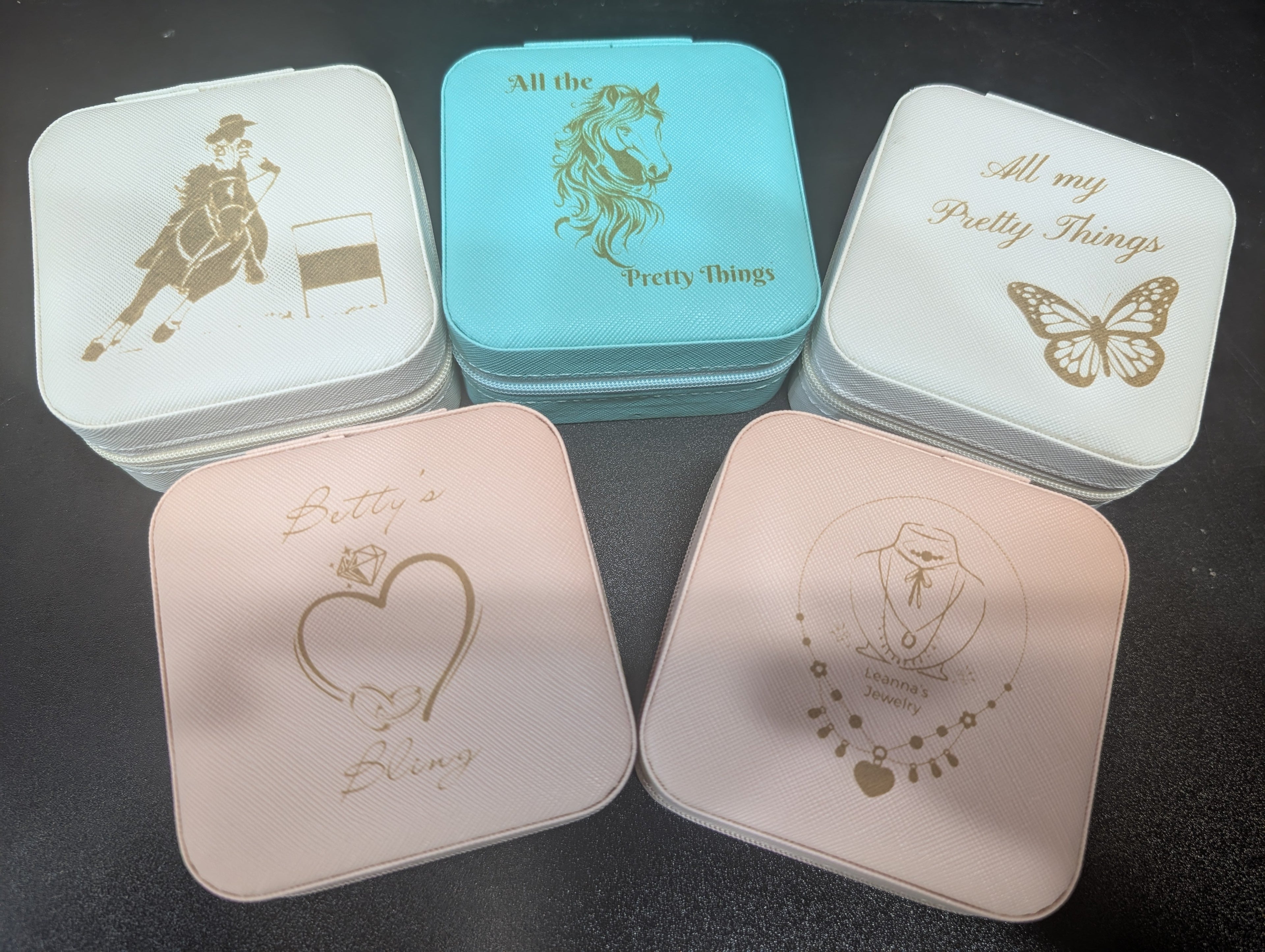 Five small square containers with gold embossed designs on a dark surface