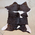 Dark brown and white calf hide rug on a floor with tile . 