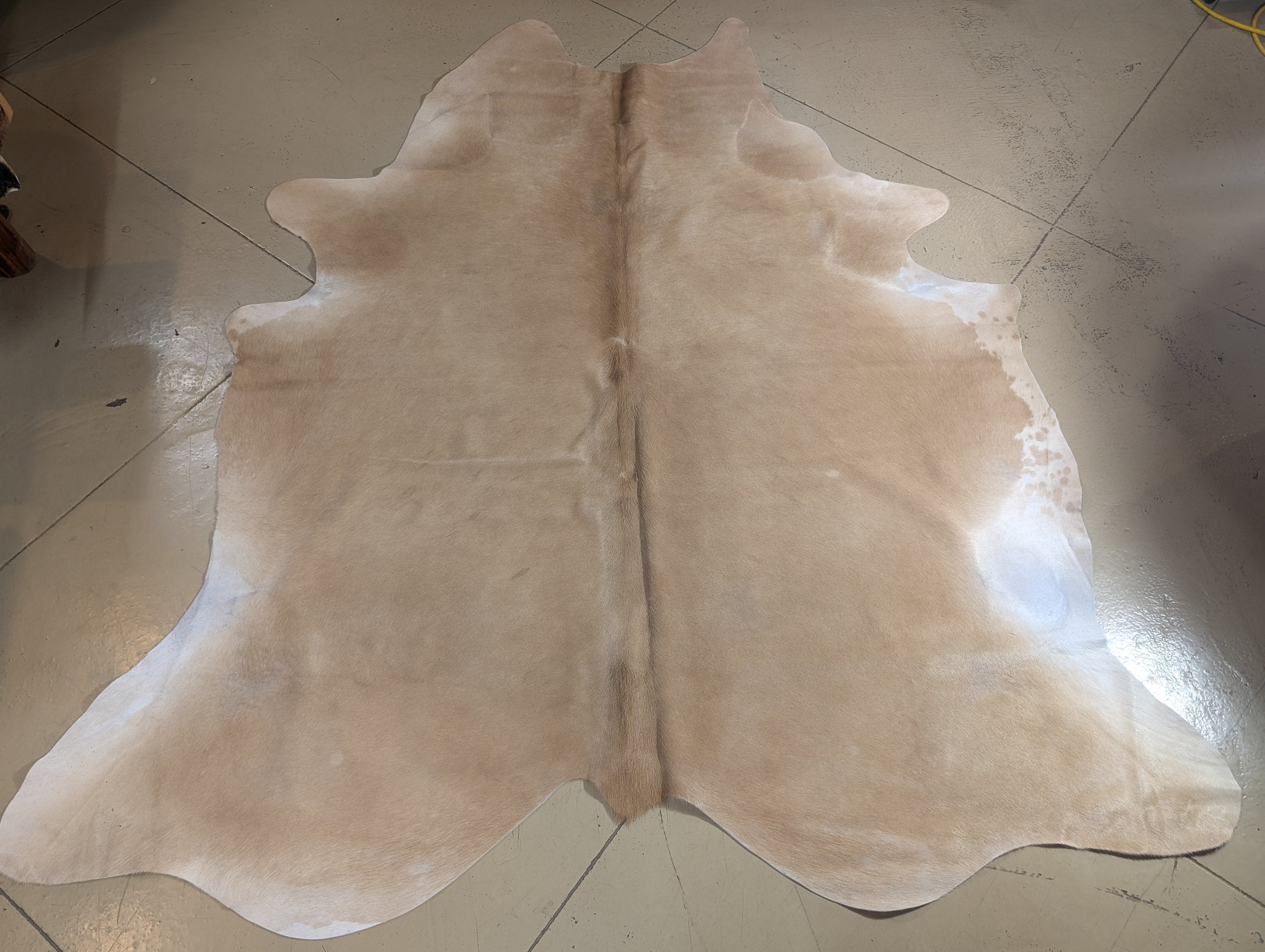 A full cowhide rug in a beige color laid out on a floor.