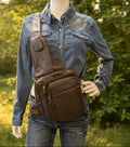 Mannequin wearing a denim shirt with a brown leather bag with trees in the back