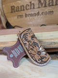 A brown genuine leather knife sheath with floral patterns displayed against a wooden background.