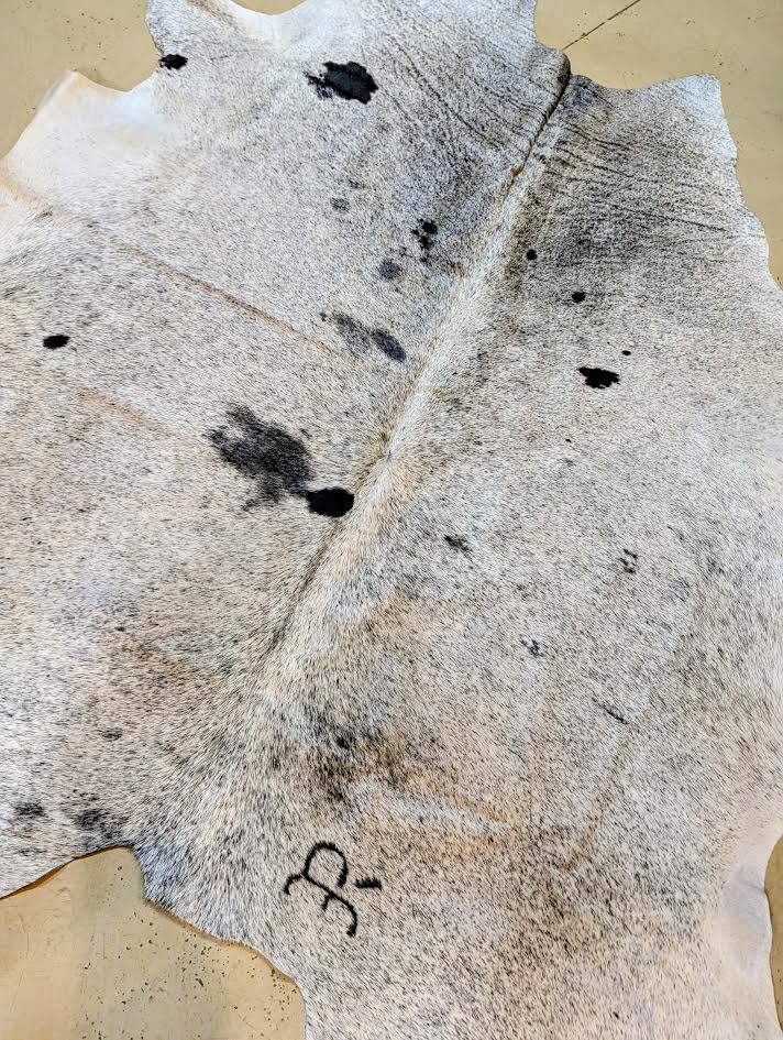 Close-up of a cowhide rug with black spots and a visible brand logo.