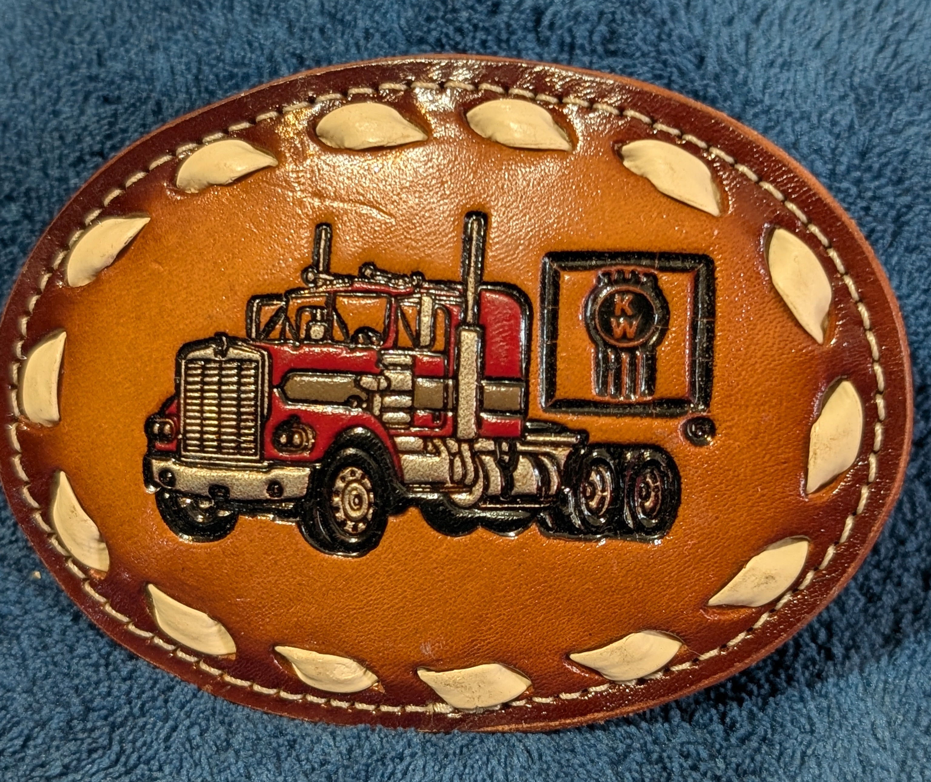 Leather belt buckle with truck design on a blue fabric background