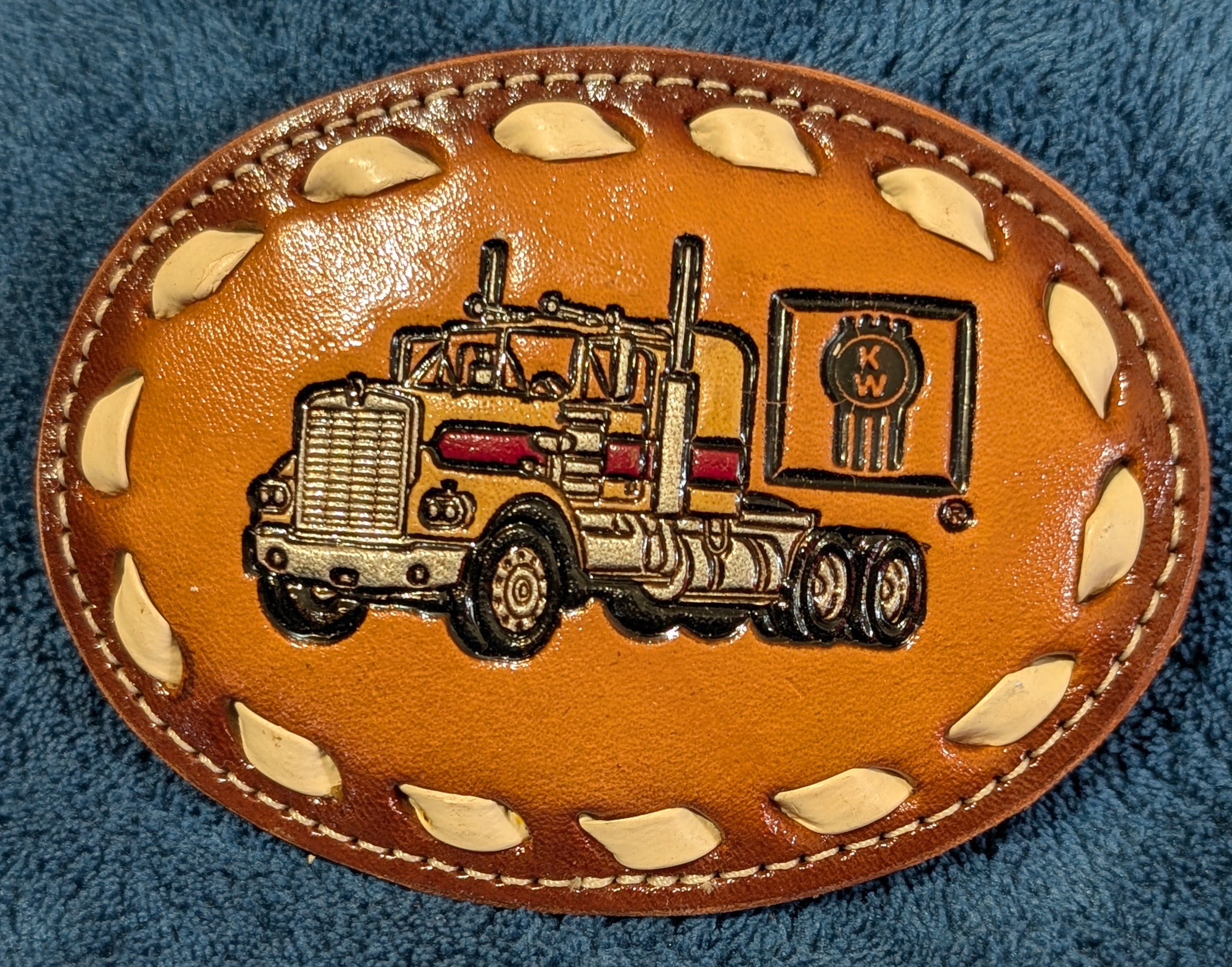 Leather belt buckle with truck design on a blue fabric background