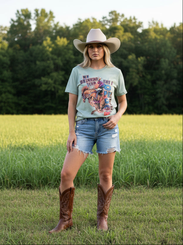 Light green t-shirt with graphic design on a lady with cowboy hat & boots in a outdoor setting.